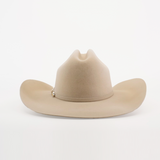 The 100X Tony Lama Belly is a beige cowboy hat made from premium beaver fur, showcasing a wide brim and top crease, with a small metallic emblem on one side. It exudes genuine Western elegance against a plain white background.