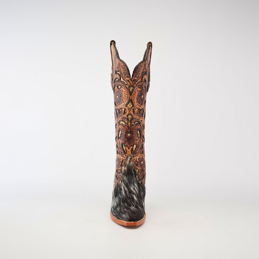 The Handtooled Cowhide Pinto boot features a tall shaft and snip toe, crafted from premium cowhide with ornate floral patterns and dark, textured heel detailing. Its rich reddish-brown color is strikingly set against a plain white background.