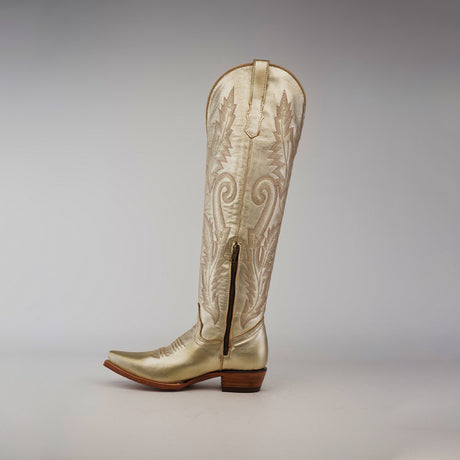 Introducing the Brittany Gold - Tall Shaft - Snip Toe: a handcrafted womens knee-high cowboy boot in metallic gold with intricate stitching, a pointed toe, and a short wooden heel, showcased on a plain gray background.