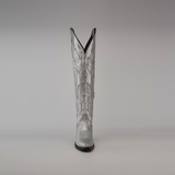 A handcrafted Brittany Silver- Tall Shaft - Snip Toe boot is highlighted against a plain gray background, showcasing premium leather with intricate stitching, a pointed toe, and a high shaft adorned with decorative patterns.