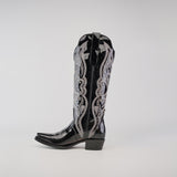 The Artemisa Patent Black cowboy boot features premium leather, intricate silver embroidery, a pointed snip toe, and a low block heel, photographed against a plain background.