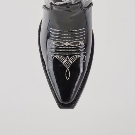 A close-up of the Artemisa Patent Black shoe reveals premium leather and intricate white stitching on the snip toe, forming elegant symmetrical patterns that highlight its craftsmanship against a plain light background.