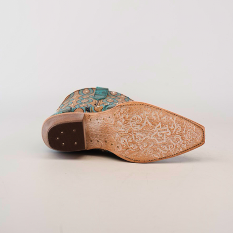 The Premier Turquoise Handtooled Flowers boot features a snip toe with a patterned sole. Its teal and brown upper showcases geometric designs reminiscent of turquoise flowers. Made from premium leather, the worn sole enhances its rustic charm.