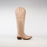 The Sara Metalic Florentine boot, with its tall shaft and snip toe, stands upright against a white background. Its beige color and decorative stitching capture the elegance of classic Western style, featuring a pointed toe and low angled heel.