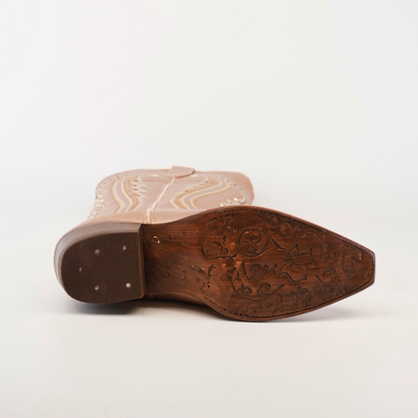 The image displays the bottom view of a tan cowboy boot on its side, showcasing a snip toe with an ornate carved sole featuring floral and abstract patterns. Light-colored decorative stitching along the side mirrors the design of Sara Metalic Florentine - Tall Shaft - Snip Toe boots.