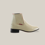 The Napa Bone - Round Toe ankle boot from our western wear collection is showcased on a white background, crafted with light-colored leather, black soles, elastic side panels, and a small red tag for style.