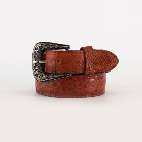 The Exotic Full Quilt Caiman - Texas Buckle - Brandy Belt showcases a brown crocodile leather design with a silver ornate Texas-style buckle, featuring intricate engravings. Rolled up, it rests against a plain white background.