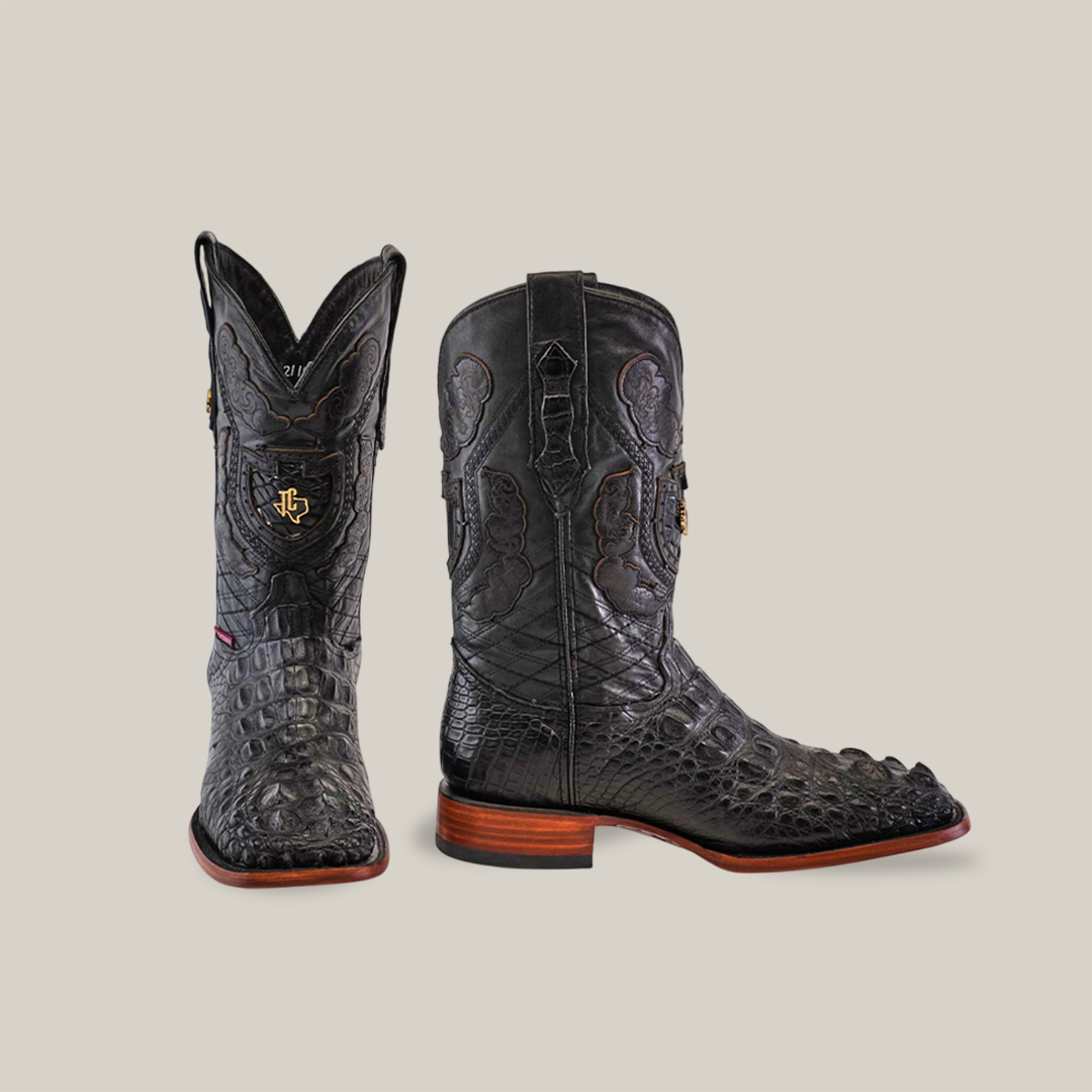 Black exotic American Alligator Head cowboy boots, named Exotic American Alligator Head - Black - Square Toe, feature a square toe, intricate detailing, wooden heel, and red sole trim. A logo emblem is displayed on the front against a beige background.