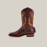 The Exotic American Alligator Hornback - Brown - Square Toe boot showcases exceptional craftsmanship with a dark brown hue, intricate patterns, and decorative stitching. It features a stacked wooden heel and reptile-skin-like textured finish, complemented by detailed cutout designs on the shaft.