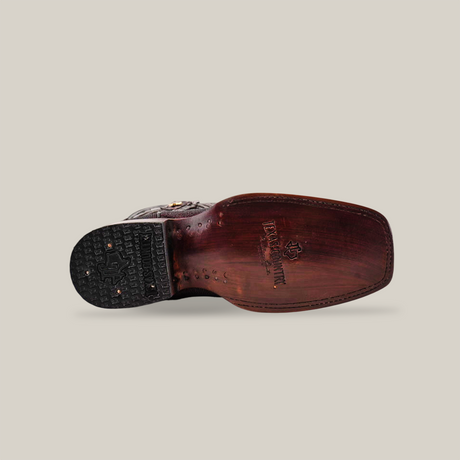 The image shows the bottom view of the Exotic Lizard - Brown - Rodeo Toe cowboy boot, with a dark sole featuring the brand logo and text. Authentic lizard skin, a squared toe, and decorative stitching emphasize its handcrafted elegance.