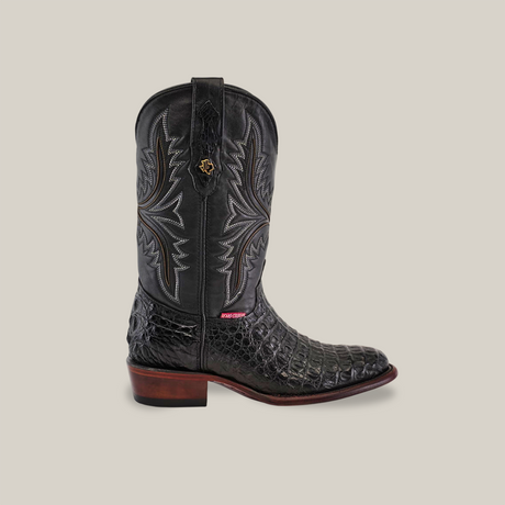 Introducing the handcrafted Exotic Caiman Hornback - Black - Round Toe boot, showcasing an intricate silver-stitched black leather with Hornback texture, a brown wooden heel, and a top pull tab. Its set against a light gray background.