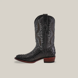 The Exotic Caiman Hornback - Black - Round Toe boot features a black design with intricate light stitching and a pattern similar to exotic Caiman Hornback. It is handcrafted and has a low brown wooden heel with pull tabs, all against a plain background.