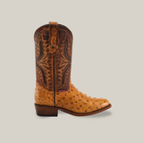 The Exotic Full Quilt Ostrich - Paja boot features Western Heritage with tan and dark brown colors, decorative stitching, and a texture that mimics Exotic Full Quilt Ostrich leather. It has a round toe, low heel, pull straps at the top, set against a plain beige background.