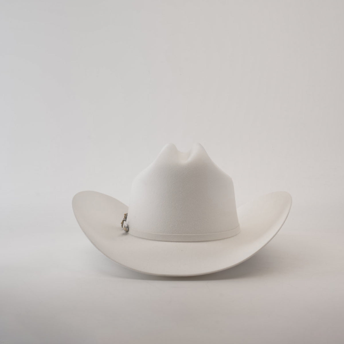 The 1000X Imperial White hat, featuring a pin on the side, is elegantly showcased against a plain light gray background, exuding timeless charm.