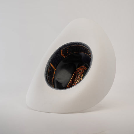 A 1000X Imperial White hat rests on its side against a plain background, revealing the dark brown and orange patterned interior with black lining, offering a glimpse of 100% genuine mink craftsmanship.