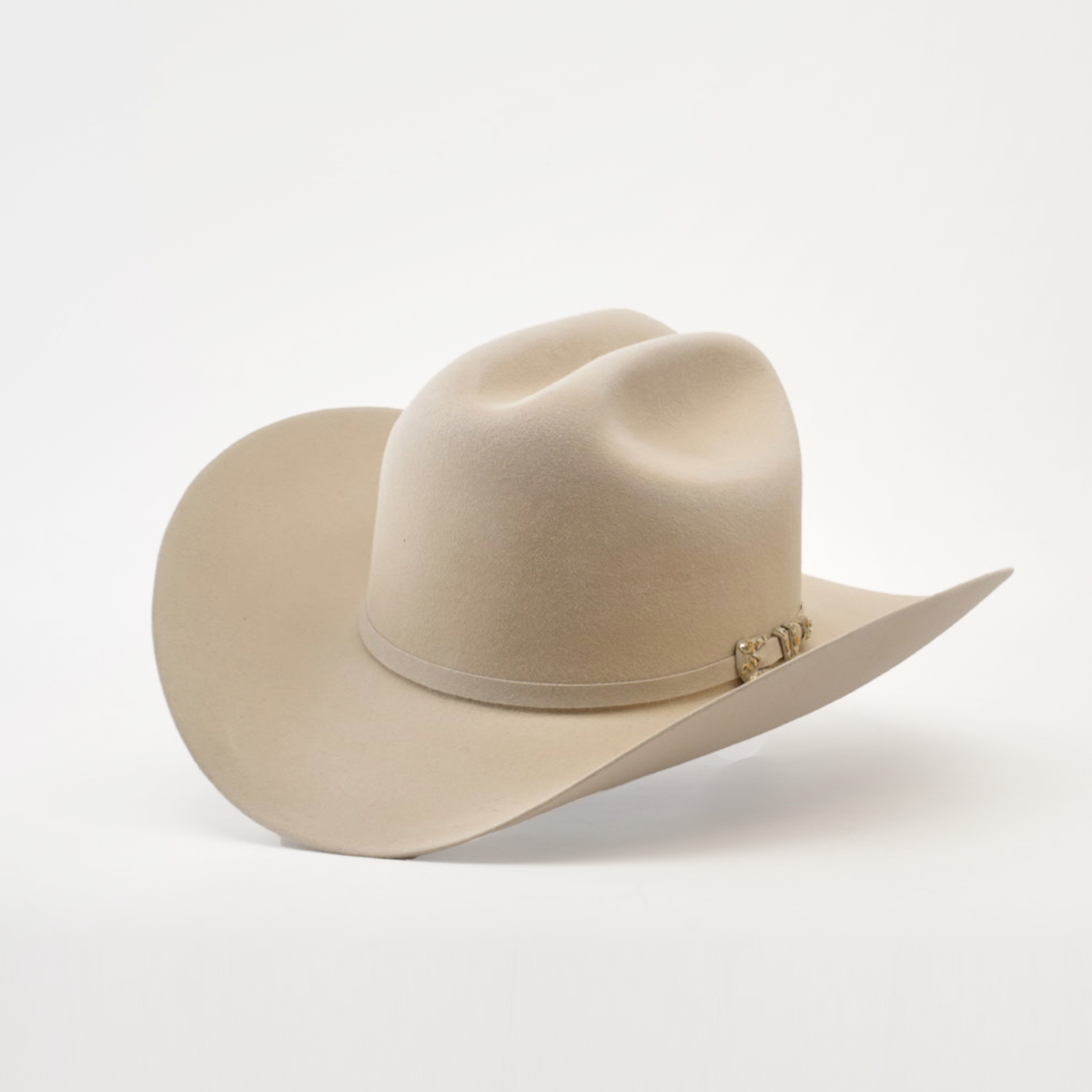 The 10X Jerarca Belly is a cream-colored cowboy hat made from luxurious fur felt, featuring a wide brim and distinctive crown crease. Adorned with a decorative metallic embellished band, this classic western headwear evokes Larry Mahans timeless style against a white backdrop.