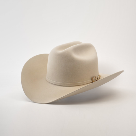 The 100X Independencia Belly, a luxury beige cowboy hat made from premium full beaver fur, boasts a curved brim and decorative band, elegantly showcased on a white surface.