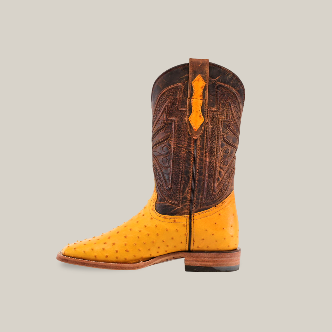 The Exotic Full Quilt Ostrich in Buttercup is a tall cowboy boot featuring a square toe, buttercup ostrich leather, and a dark brown leather upper with intricate stitching, set against a plain beige background.