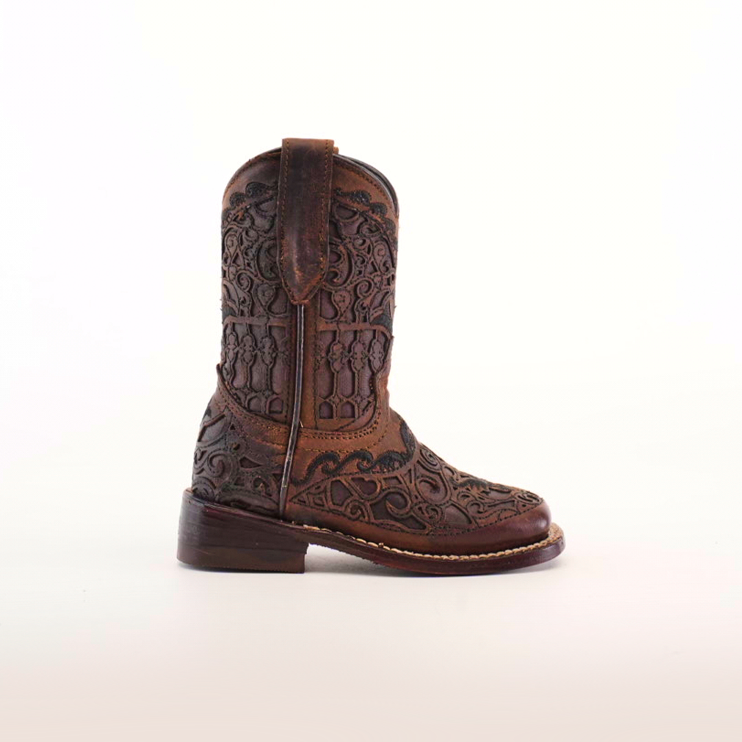 The Taurine Matte Chocolate Square Toe boots feature intricate floral and geometric patterns etched into premium leather, showcasing western elegance. The ornate design highlights exceptional craftsmanship against a light background, making these boots a classic choice.