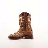 The Margacruz Studs Orix - Square Toe is a mid-calf, low-heel girls cowboy boot crafted from premium brown leather with intricate white floral embroidery against a plain background, adding a touch of Western charm.