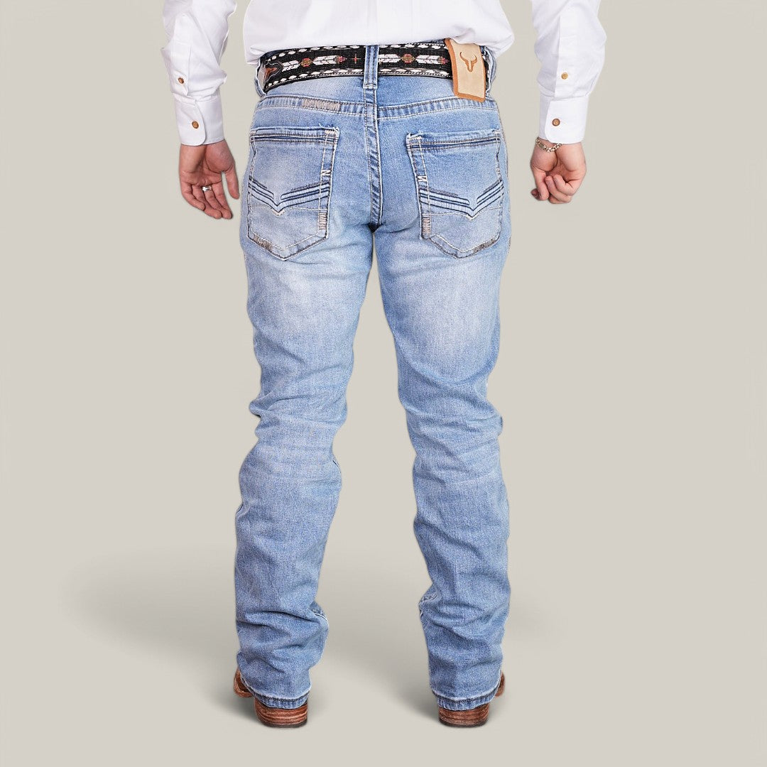 Someone wearing Western Blue Straight Fit Embroidered Jeans - W434, a white shirt, and a patterned black belt is facing away. The jeans feature a distinctive stitched pattern on the back pockets. Brown shoes are visible against the plain light gray background.