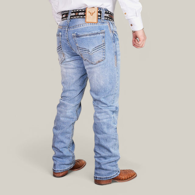 A person wearing Western Blue Straight Fit Embroidered Jeans - W434 and a decorative belt stands against a plain background, sporting a white long-sleeve shirt and brown textured shoes, with the blue jeans adding subtle Western flair.