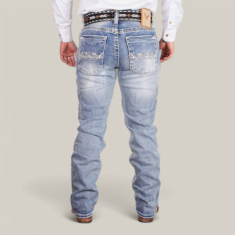 The individual is wearing Western Blue Straight Fit Embroidered Jeans - W430 featuring white stitching, a decorative belt, pockets, and a leather patch. They pair the jeans with a white long-sleeve shirt and brown shoes while standing on a plain background.