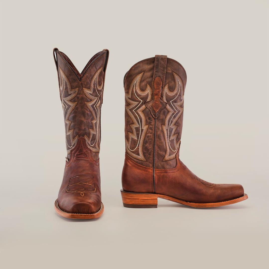 The Fresno Cogñac - Wide Cutter Toe cowboy boots feature intricate stitching, a wooden heel, and pointed toes. The right boot stands upright while the left is angled, reflecting the cowboy lifestyle on a plain white background.