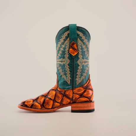 The Big Bass Pirarucu Print Tan - Square Toe cowboy boots feature a meticulous design, expertly handcrafted. Their teal upper boasts detailed stitching, while the lower showcases a striking Big Bass Pirarucu print on cowhide leather, all epitomizing rugged elegance and artisanal charm against a white background.