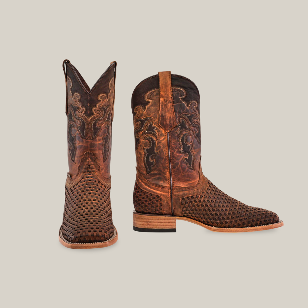 These premium cowhide cowboy boots in Texas Basket Weave Matte Brown showcase intricate stitching, a wooden heel, and a tall shaft with ornate designs. The Square Toe boots are displayed with one upright and the other artfully angled.