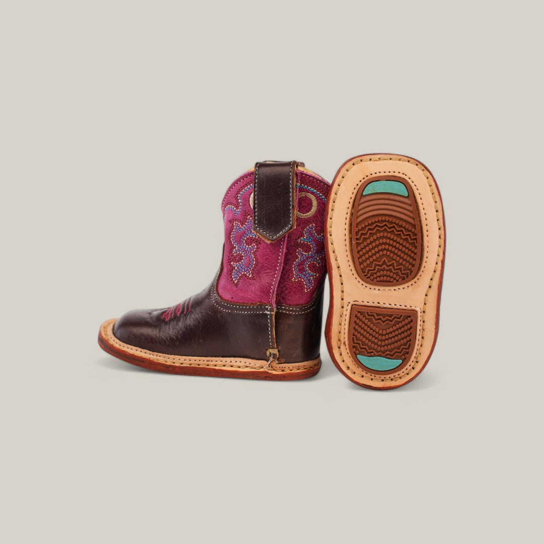 Introducing the Emma Baby Boot, a stylish addition to your little ones wardrobe. These toddler-sized boots feature a dark brown and violet design with decorative stitching and a square toe. One boot stands upright while the other lies on its side, highlighting its sole with blue accents.