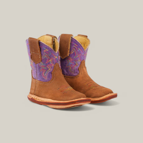 The Lilly boots, crafted from camel suede with square toes and adorned with purple and pink embroidery on the shaft, stand proudly against a light gray background.