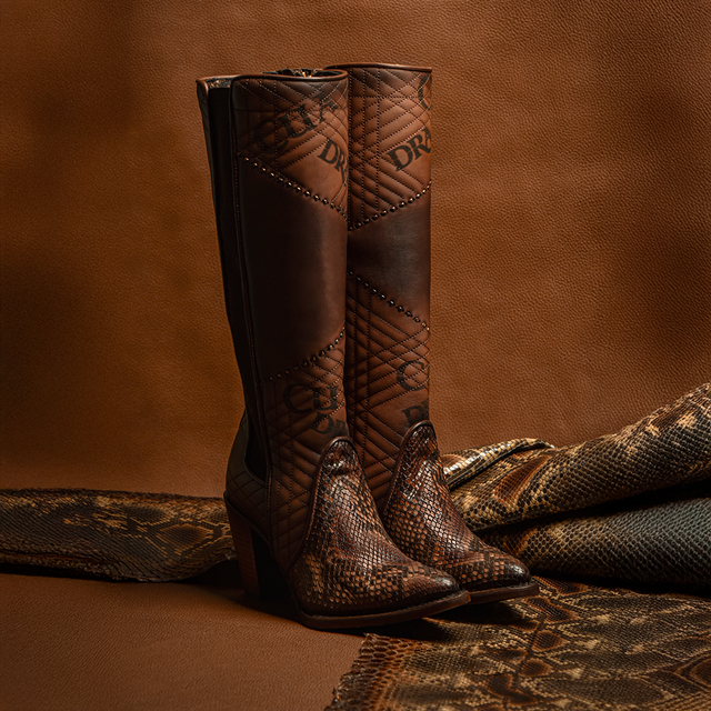 Displayed against rich brown fabric, the Glazed Chestnut Python Laser & Embroidery & Woven boots feature genuine python leather with intricate stitching and a reptile texture. These premium quality boots offer a high heel and decorative patterns for a luxurious and stylish touch.