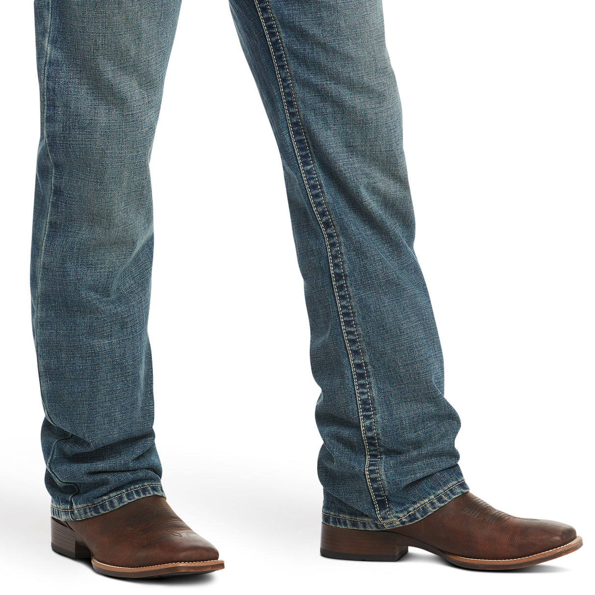 Wearing M4 Low Rise Boundary Boot Cut Jeans in Gulch and brown leather cowboy boots, a pair of legs is posed against a white backdrop. The slightly faded cotton denim features a relaxed fit with straight legs, while the boots boast low heels and rounded toes.