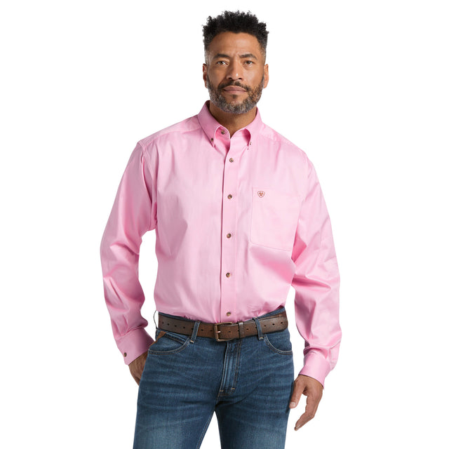 A man in a Solid Twill Classic Fit Shirt Pink (10016692) with a chest pocket and blue jeans stands confidently. The shirt has a small logo on the pocket. He sports a short beard and mustache, with his hands near his waist.