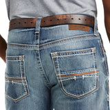 Wearing M4 Low Rise Coltrane Boot Cut Jean - Durango (10017511), featuring heavy-duty cotton denim with detailed stitching, stitch-patterned back pockets, a leather label, and accessorized with a brown leather belt. The shirt is partially tucked at the waist.