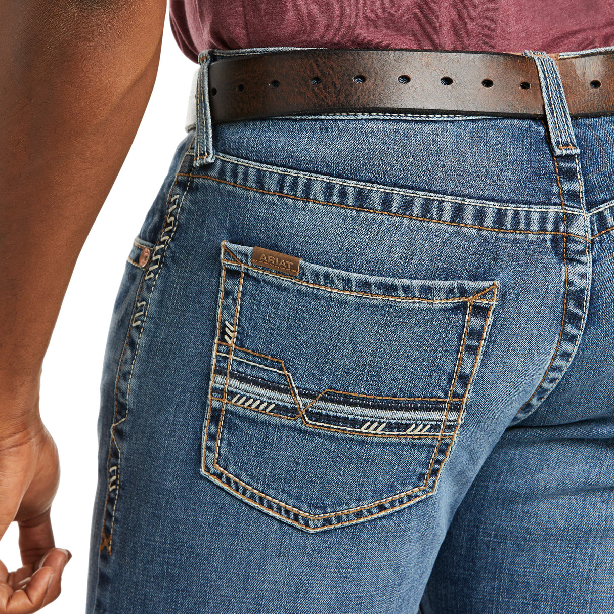 Close-up of a person in M5 Slim Stretch Stillwell Stackable Straight Leg Jean - Fargo with detailed back pocket stitching, crafted from premium cotton, secured by a brown leather belt. A maroon shirt is neatly tucked into the jeans.