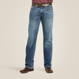 Wearing M5 Slim Stretch Stillwell Stackable Straight Leg Jean - Fargo, paired with brown leather boots, a brown belt, and a maroon shirt, a person stands against a plain background. The faded jeans offer a worn-in look for both comfort and style.