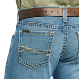 A person wears blue M7 Slim Stretch Julian Straight Jeans - Hartwell by Ariat, featuring a brown leather belt. The modern cowboy style is enhanced with decorative back pocket stitching and an Ariat tag. A green shirt peeks above the waist, completing the ensemble.