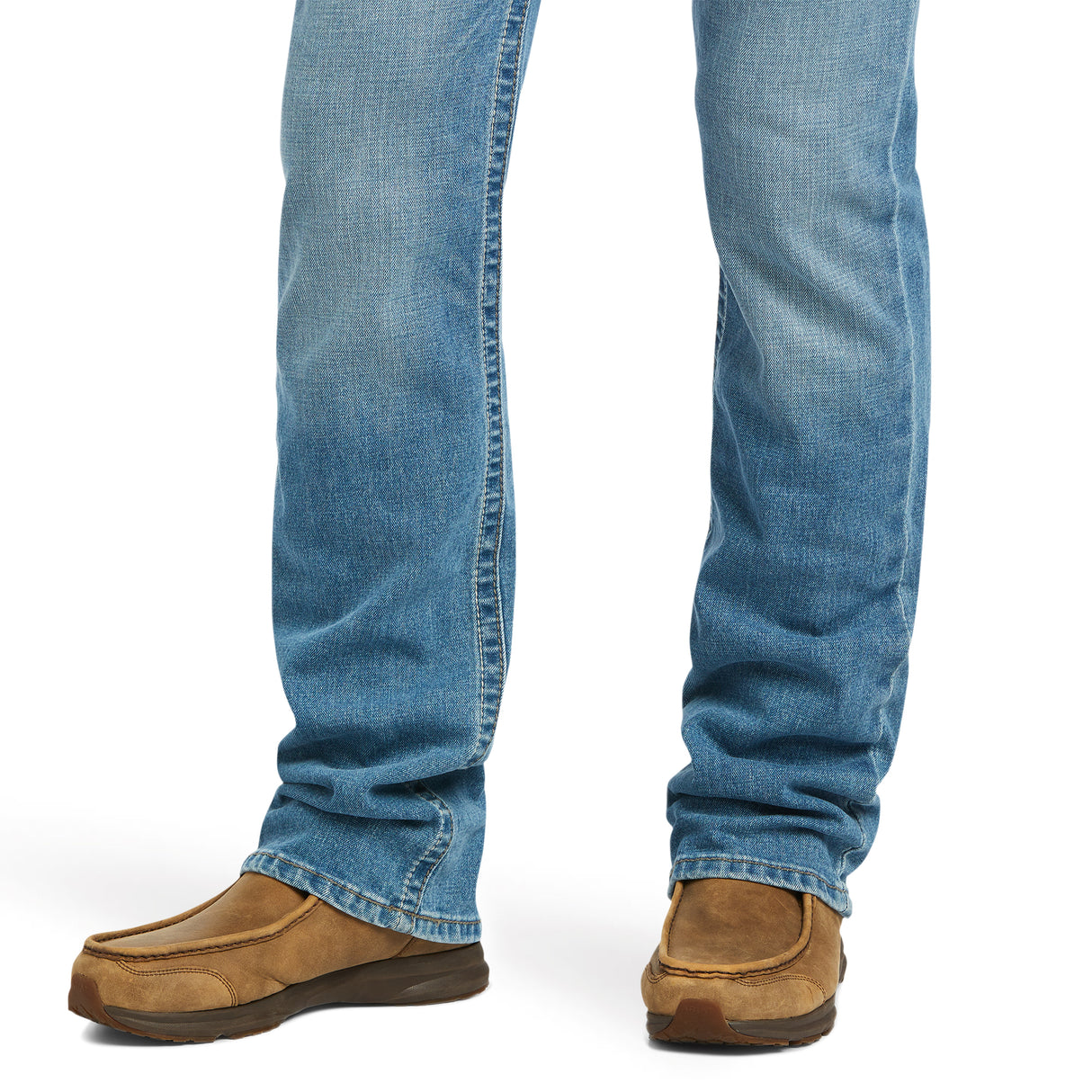 A close-up shows a person wearing M7 Slim Stretch Julian Straight Jeans - Hartwell 10039614 in light blue with brown slip-on shoes. The jeans are straight-cut, creating a modern cowboy vibe, while the shoes appear slightly worn. The focus is on the lower legs and feet against a plain white background.