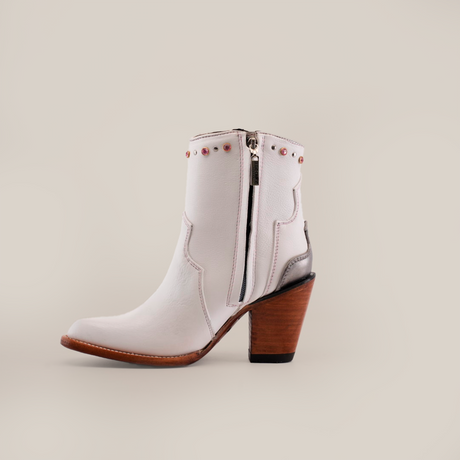 The Milan Chains Bootie Frost White - J Toe, part of the Platinum Collection, stands out against a plain white backdrop. Crafted from premium leather with a side zipper and wooden heel, it features decorative metal studs along the top edge.