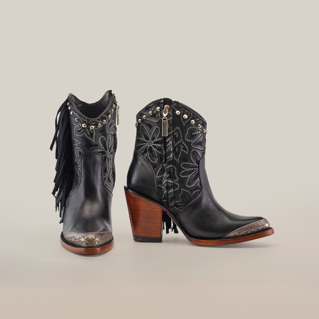 Meet the Dallas Fringe Bootie Black - J Toe, a pair of black leather ankle boots with wooden heels, adorned with silver studs and floral embroidery. One boot features side fringe detailing, complemented by metallic accents on the toes for an extra touch of luxury.