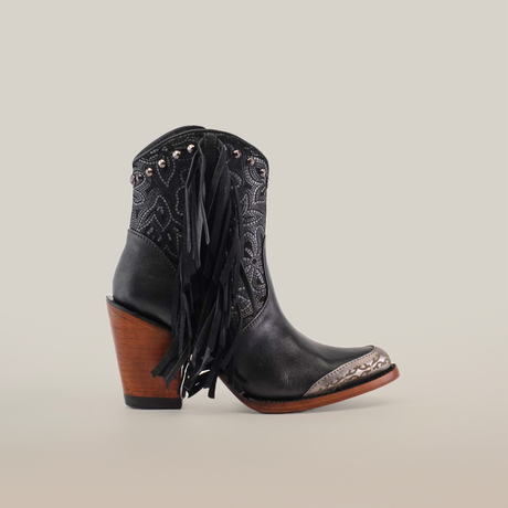 The Dallas Fringe Bootie Black - J Toe features premium leather, a single black cowboy boot with intricate patterns, a metal toe cap, and black leather fringes on the sides. It boasts a stylish brown wood heel against a plain white background—a true showcase of luxury craftsmanship.