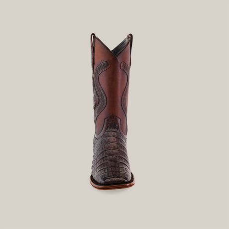 A front view of a single brown cowboy boot from the Platinum Collection, featuring an exotic Caiman belly texture on the lower part and decorative stitching on the upper shaft. The boot stands against a plain beige background, exemplifying Western fashions timeless allure. Product: Exotic Caiman Belly Tail - Diamond - Tabaco - Square Toe.