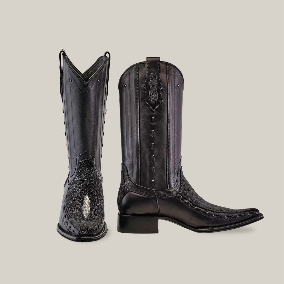 A pair of Exotic Stingray - Platinum - Black - Versy Toe boots, showcasing elegant intricate stitching and decorative tooling. One boot stands upright, the other lies down to display their unique design and shine against a plain white background.