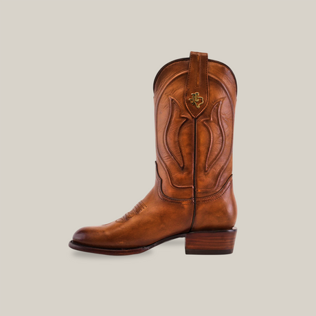 The Western - Platinum - Honey - Roper Toe cowboy boot, with a brown leather finish, intricate stitching, and a roper toe design, features a raised heel, pull tab, and decorative emblem. It stands out vividly against the plain white background.