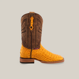 The Exotic Caiman Horn Back - Buttercup-Square Toe boot features a side view with a brown, intricately stitched upper and bright yellow caiman leather-textured foot. The luxurious design includes a wooden heel and dark sole, capturing the cowboy lifestyle against a plain backdrop.