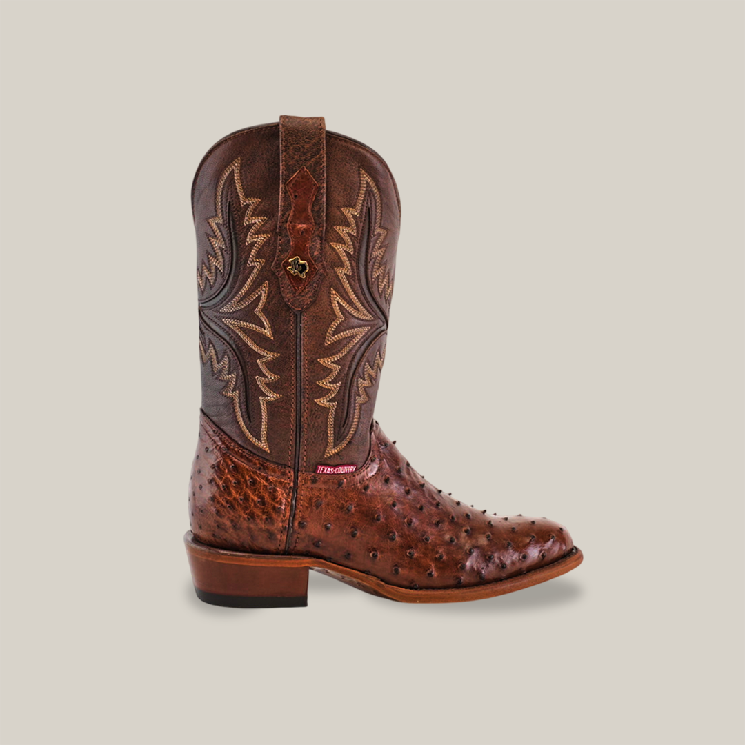 The Exotic Full Quilt Ostrich Boot in Brown showcases intricate leather artistry with detailed stitching and a textured pattern like ostrich skin, complemented by pull straps and a low heel, elegantly set against a plain light background.