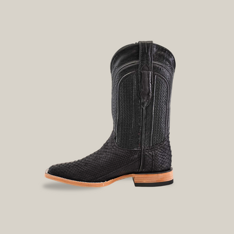 The Exotic Python in Matte Black showcases a captivating python leather texture with a square toe and a light brown sole. Displayed facing left on a neutral background, this western-style boot stands out in style.