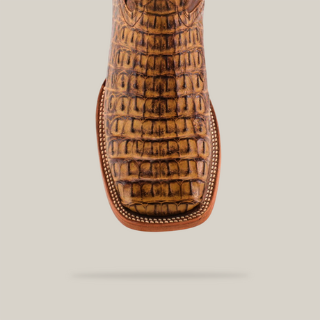 An Exotic Caiman Horn Back - Antique boot, featuring a square toe and genuine caiman leather, is centered on a light gray background. Its textured brown reptile-like surface and detailed stitching exhibit the craftsmanship of skilled artisans.